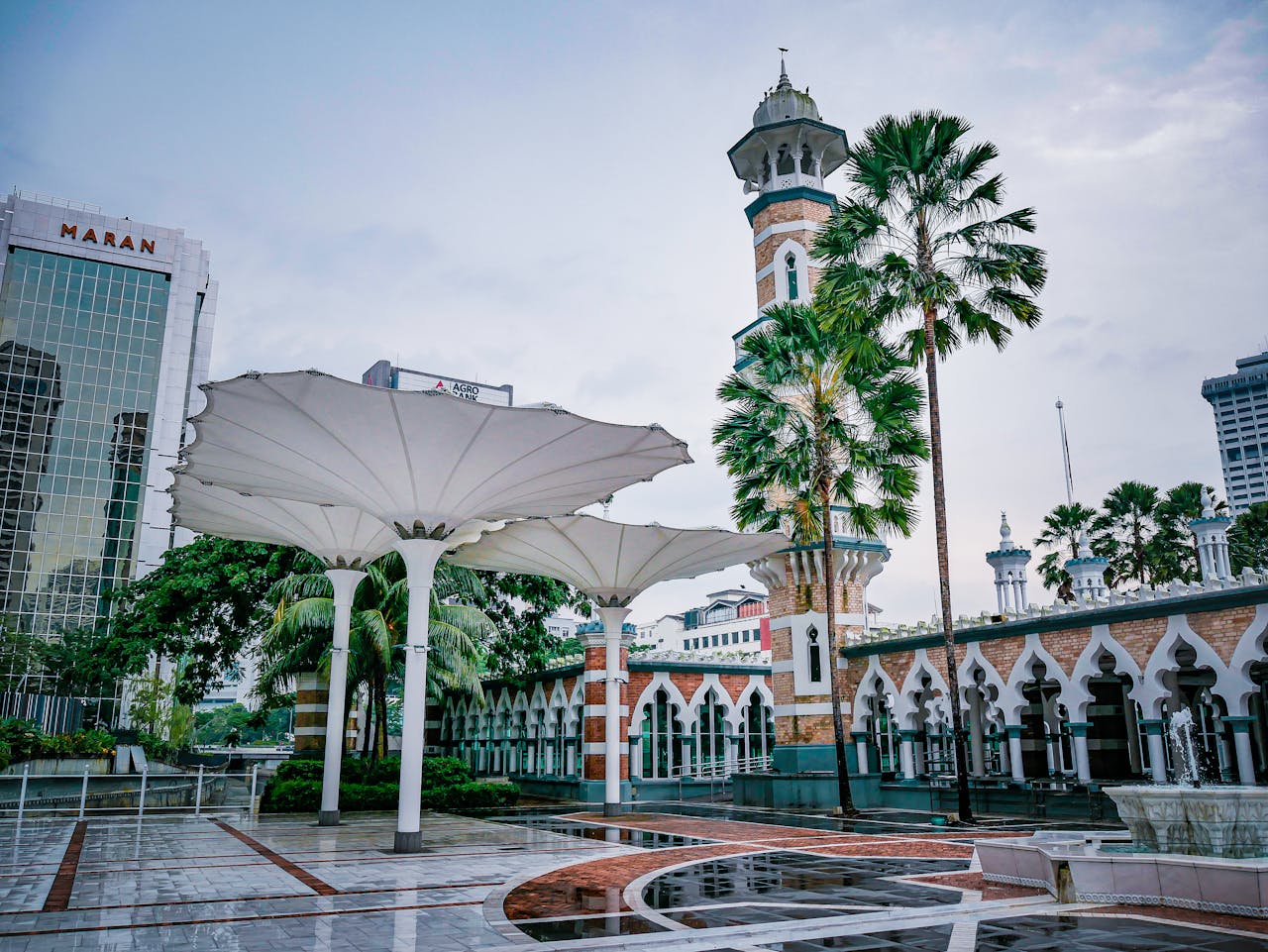 View of Jamek Mosque with lush palm trees and modern architectural elements in Kuala Lumpur, Malaysia.