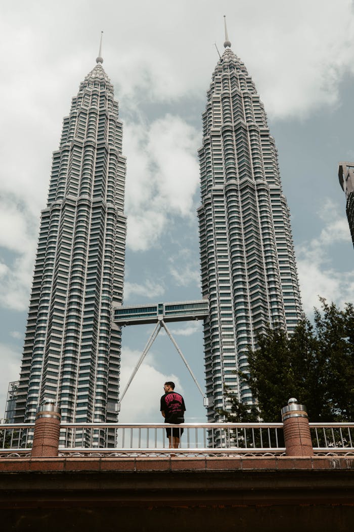 A person admires the stunning Petronas Towers in Kuala Lumpur under a clear sky.