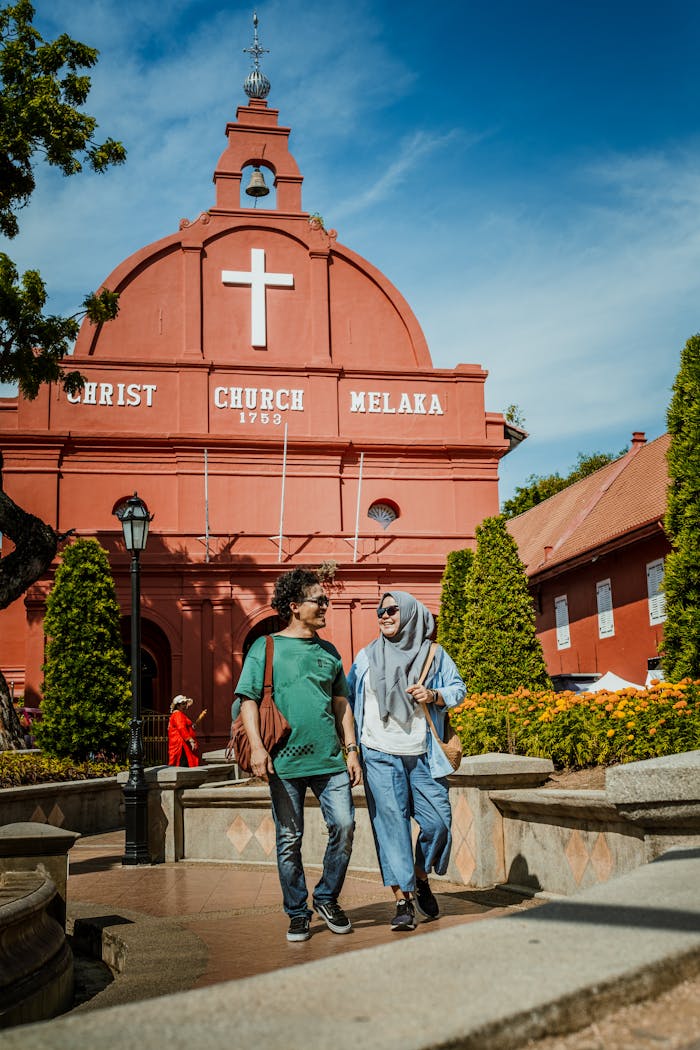 A young couple walking in front of the historic Christ Church in Malacca, Malaysia.