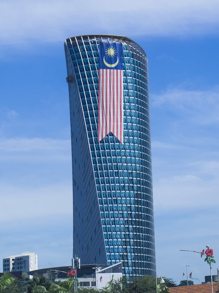 ours-journey Modern skyscraper in Kuala Lumpur with the Malaysian flag against a clear blue sky.